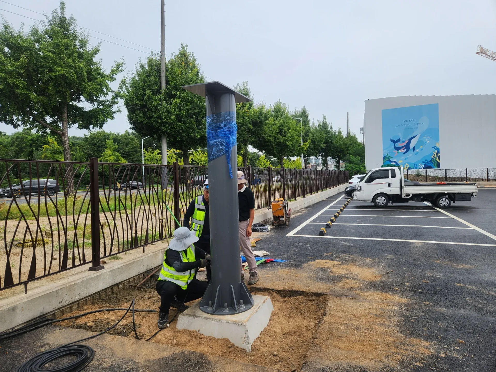 학교 교내 주차장에 세워진 지주형 전광판 지주와 배경의 학교 건물 벽화