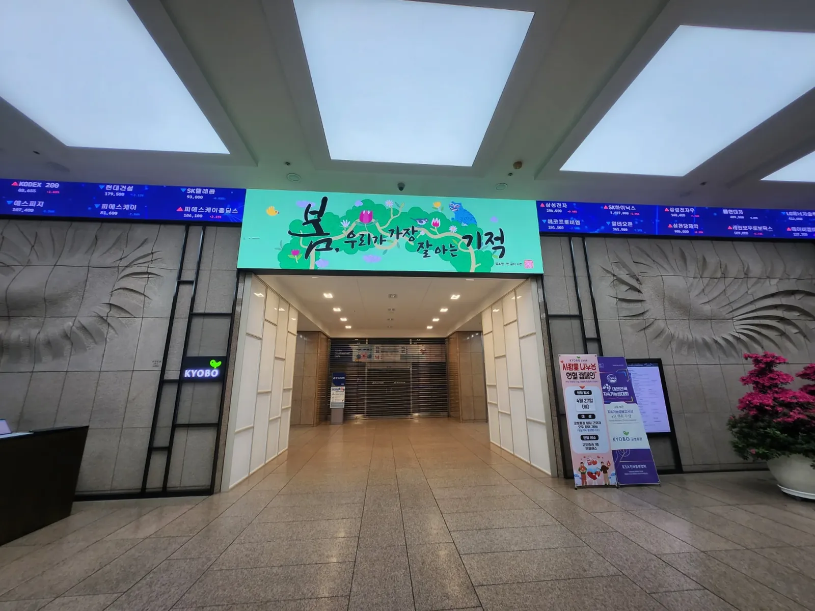 증권사 로비 입구 양옆에 설치된 주가지수 표시 LED 전광판과 계절 홍보 배너